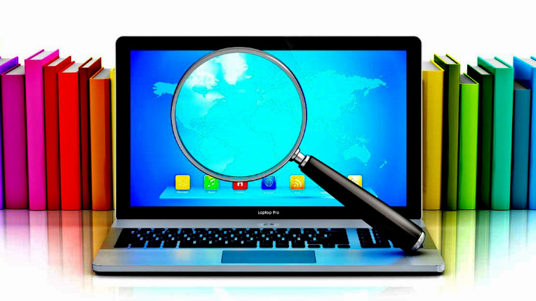 a laptop with a magnifying glass on the screen with vertically stacked books behind