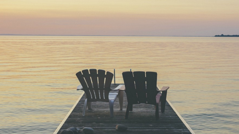 two chairs on the end of a dock looking out on a lake